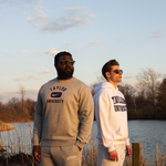 Two men posing with Taylor University apparel on with pond behind them.