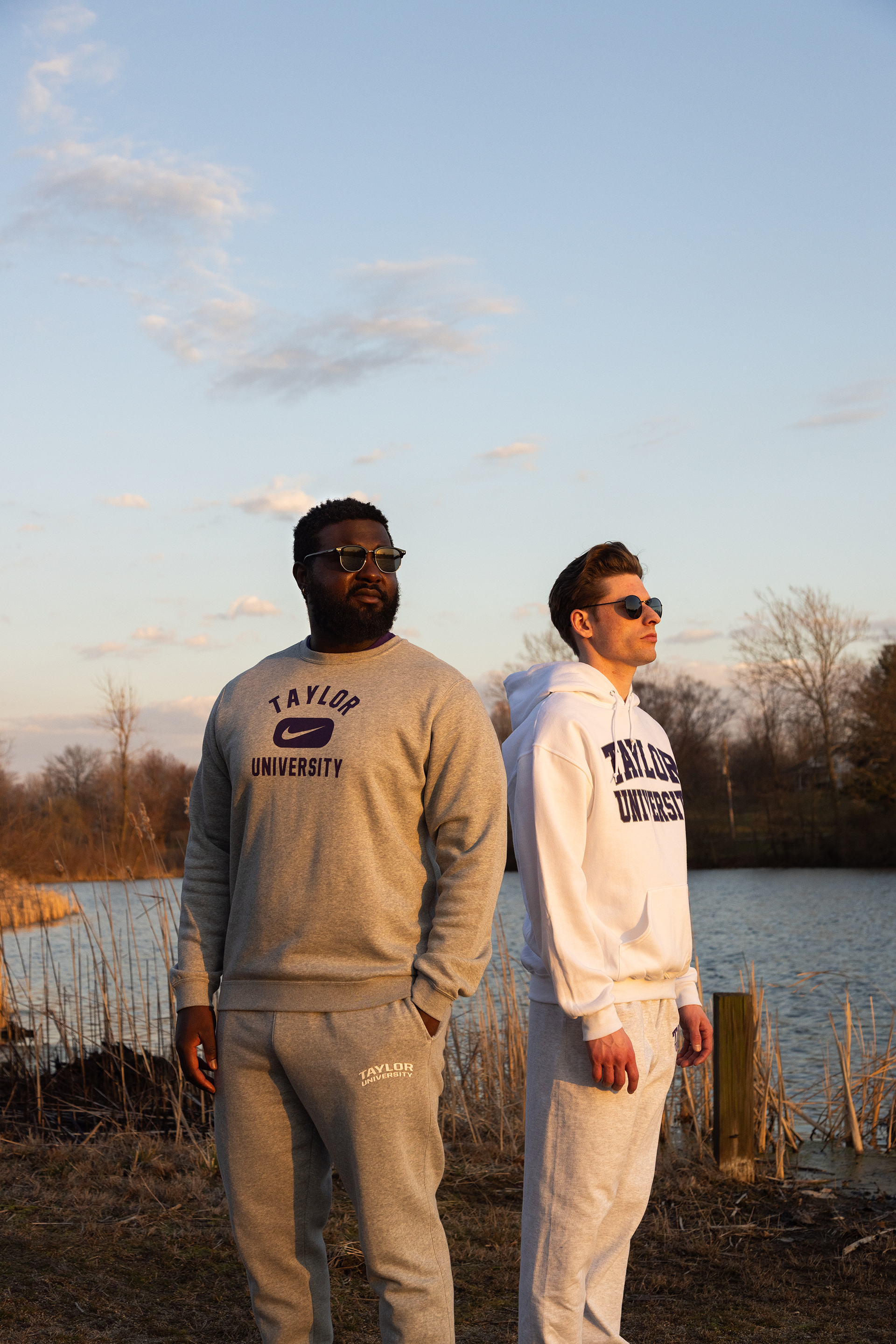 Two men posing with Taylor University apparel on with pond behind them.