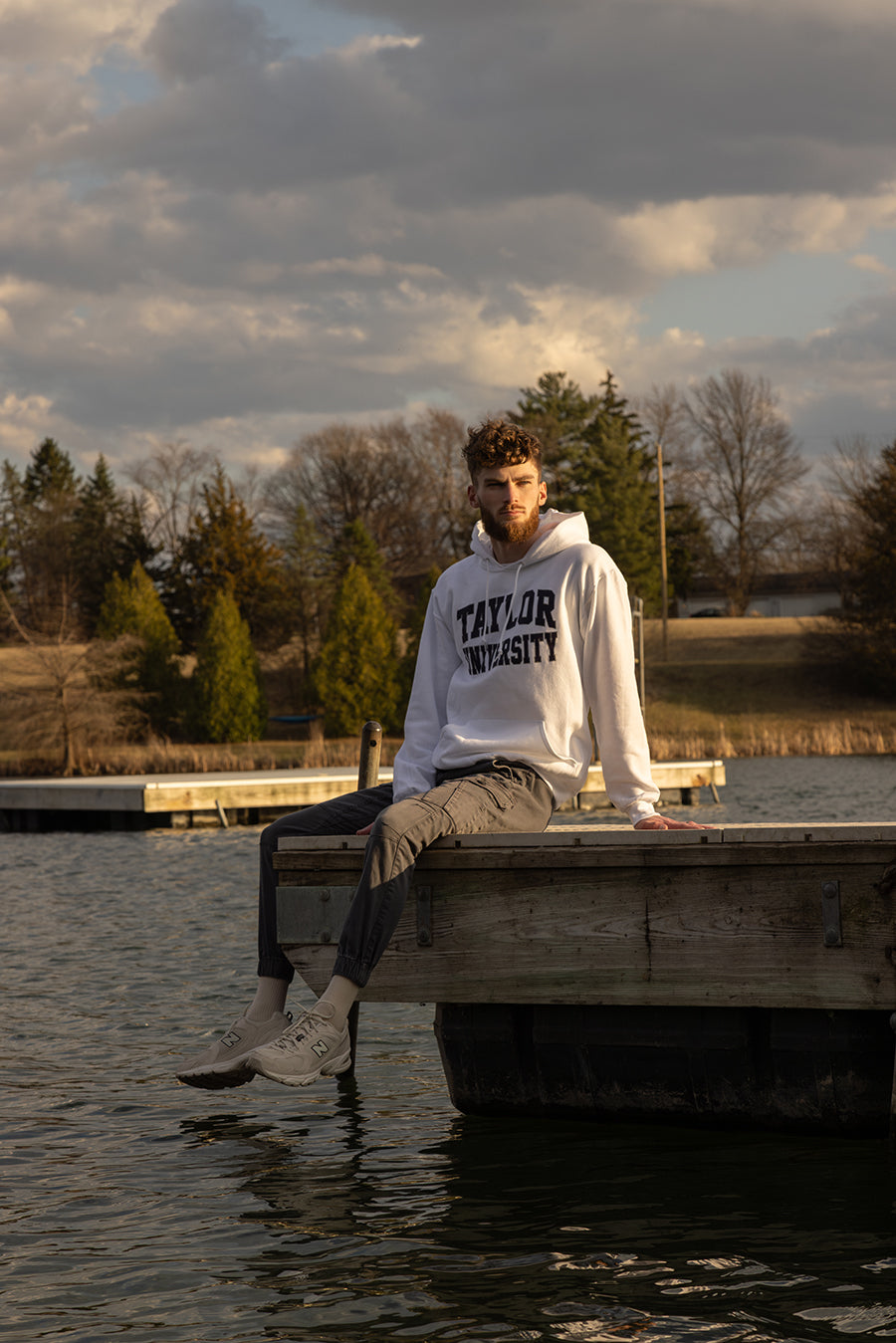 Male sitting on a dock in the water wearing a Taylor University hoodie.