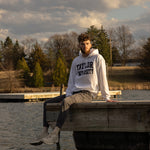 Male sitting on a dock in the water wearing a Taylor University hoodie.