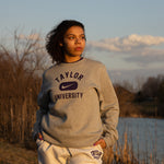 Girl posing in Taylor University apparel with trees and pond behind her.
