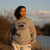 Girl posing in Taylor University apparel with trees and pond behind her.