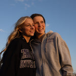 2 Girls posing with the sky behind them wearing Taylor University hoodies. 