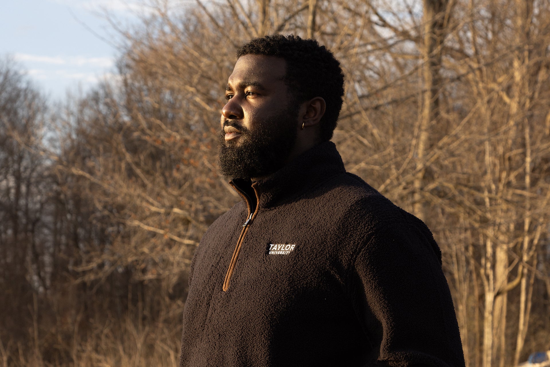 Male posing in front of trees wearing Taylor University 1/4 zip.